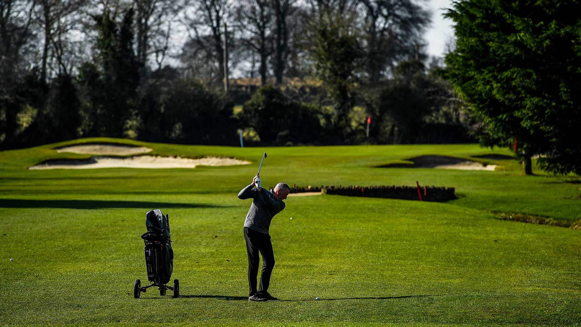 man swings tee shot golf course