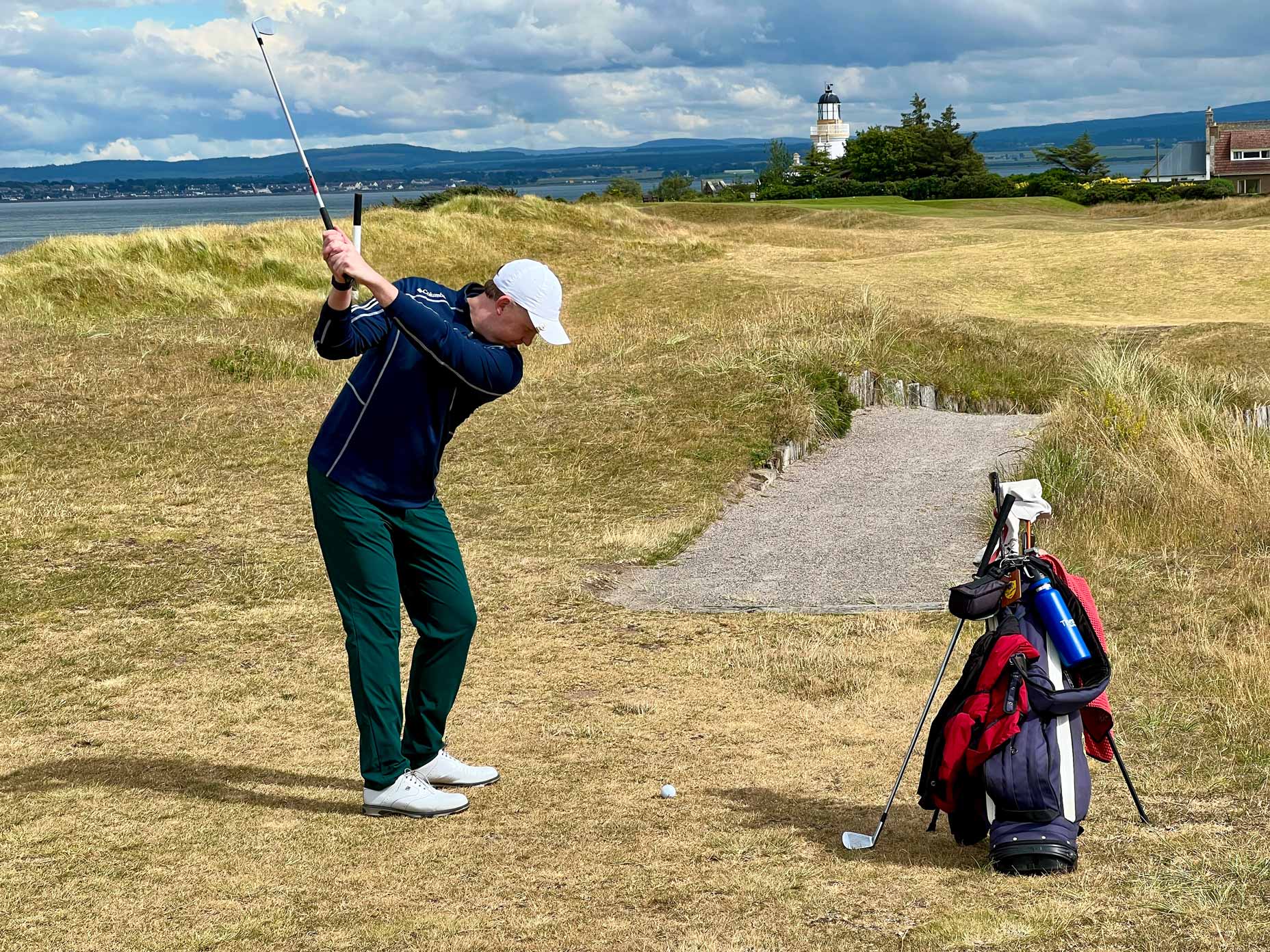 A golfer hits a shot down an undulating fairway.