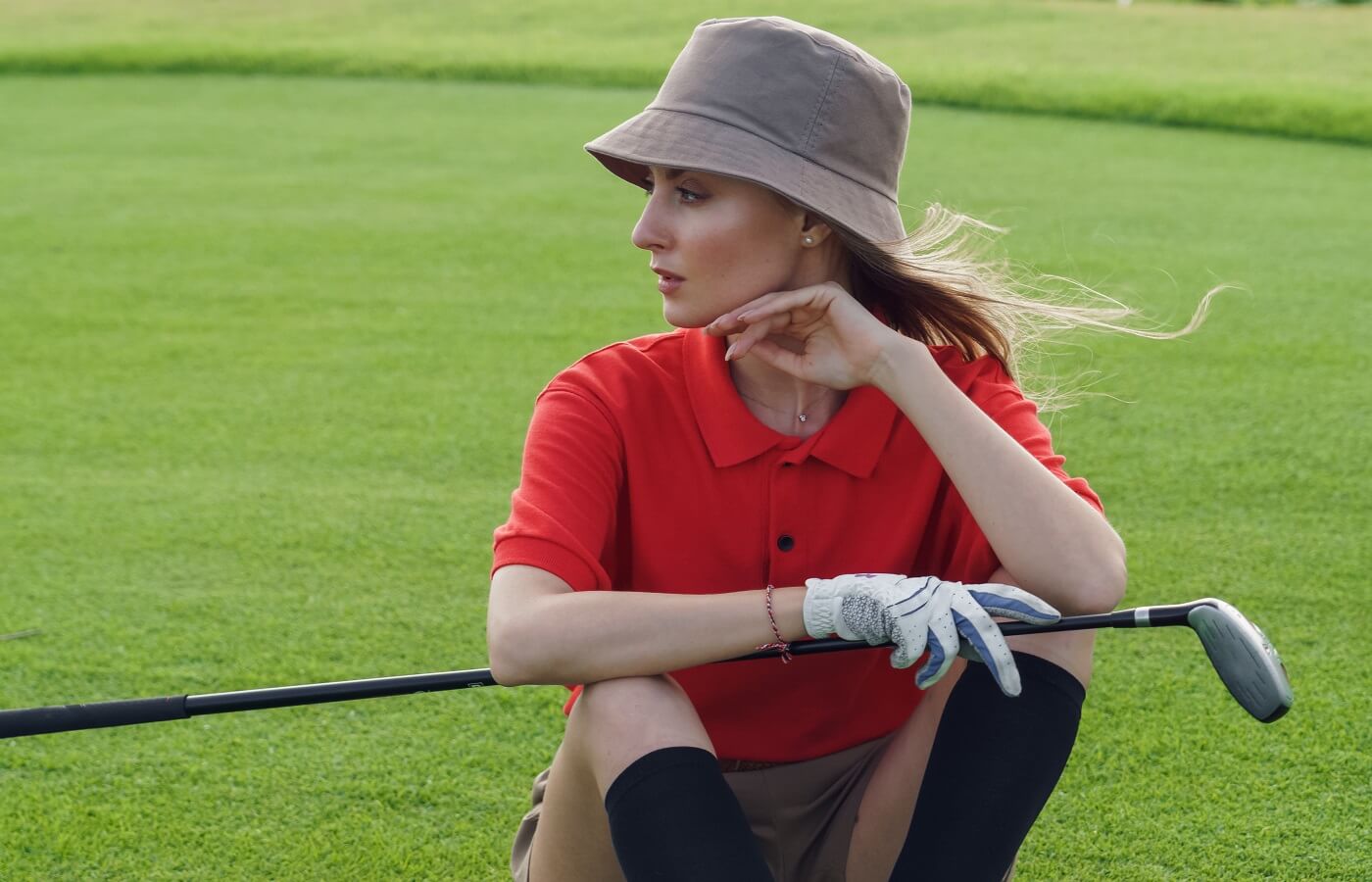 Woman golfer sitting on the green wearing a bucket hat