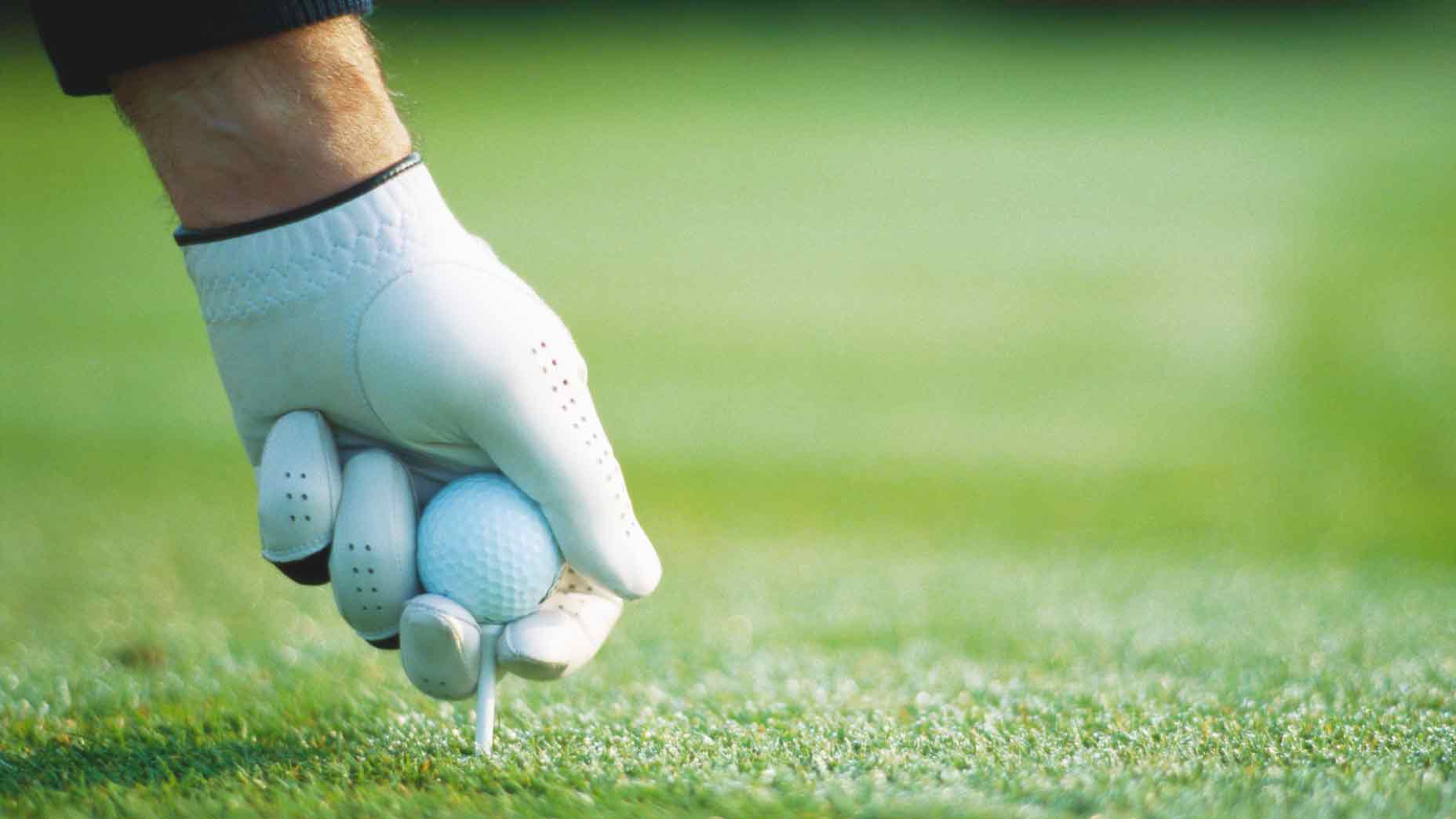 Golfer sticks tee into ground with golf ball on top at golf course