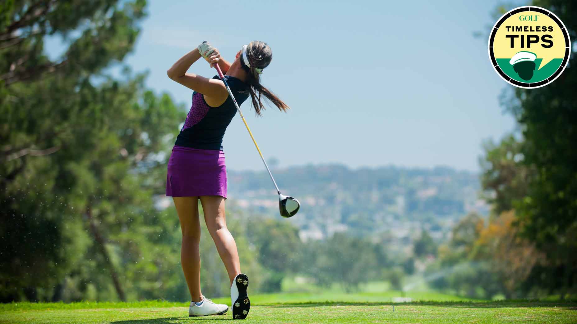 female golfer hits driver onto a fairway down below with blue sky in the distance