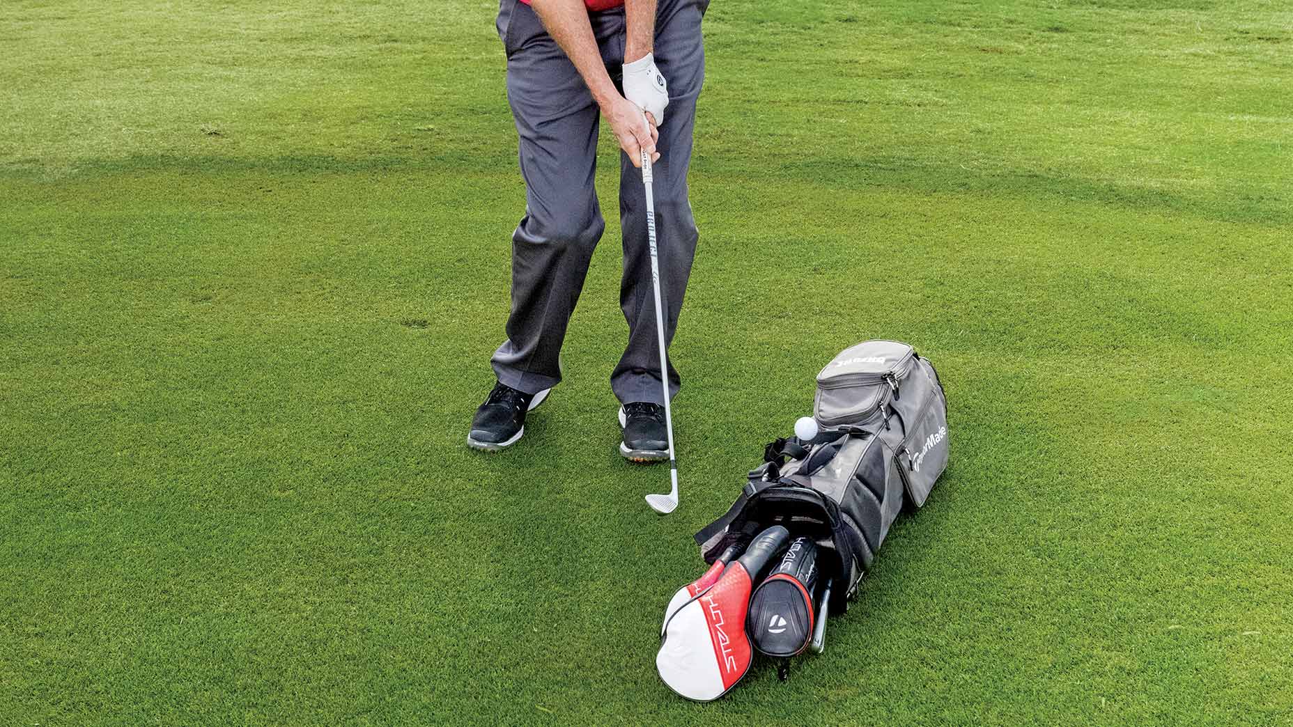 a golf teacher chips over a golf bag