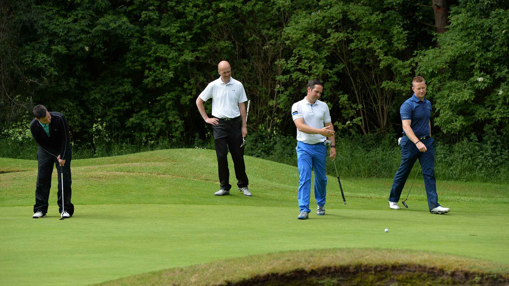 four golfers standing on a green as one golfer putts