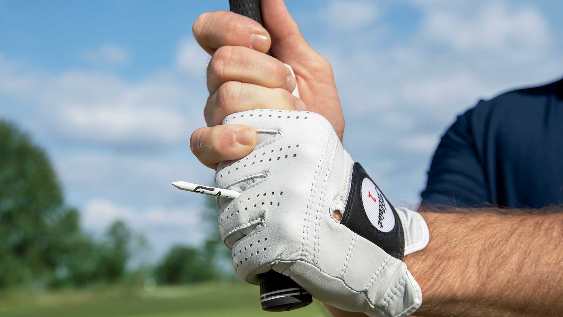 a golfer holds a tee between a golf glove